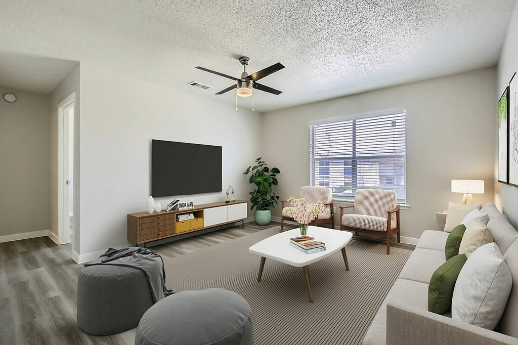 A living room with a grey sofa, a wooden coffee table, a flat screen TV, a potted plant, and a ceiling fan.