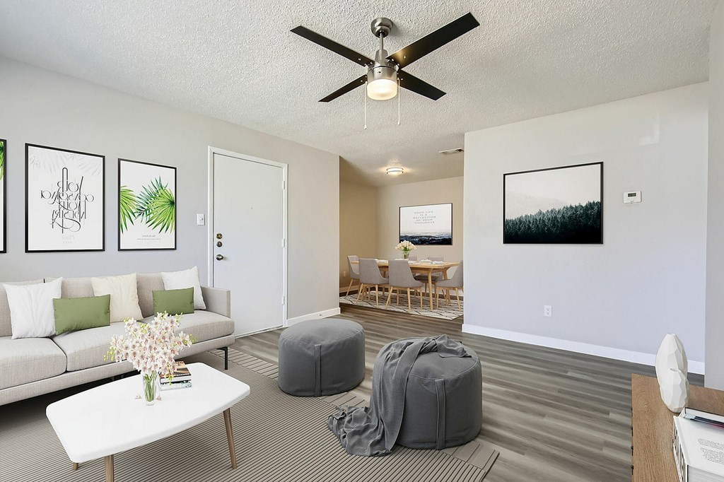 A living room with a white couch, a coffee table, a ceiling fan, and a dining area in the background.