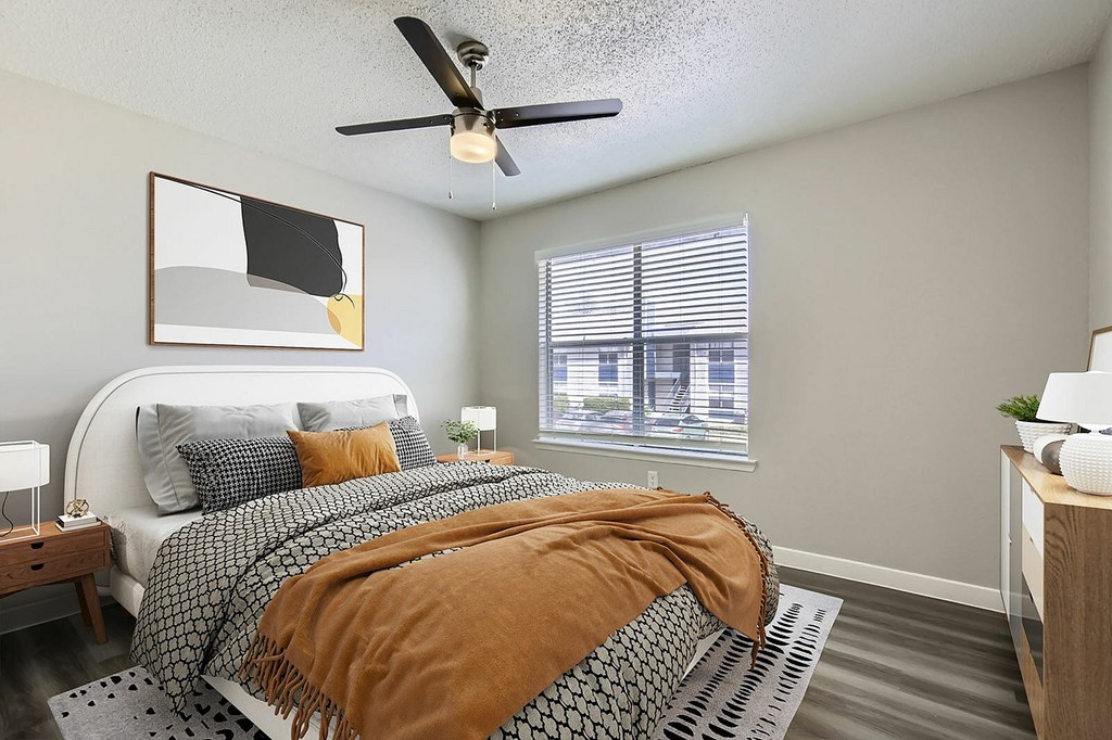 A bedroom with a bed covered in a brown blanket and a ceiling fan above it.