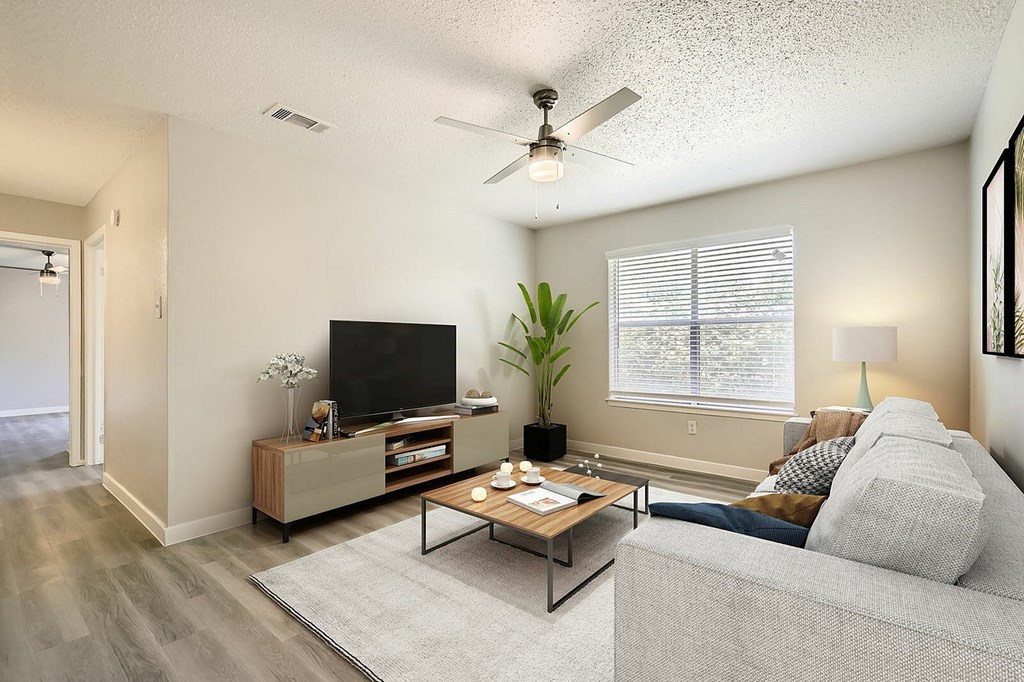 A living room with a grey couch, a wooden coffee table, a flat screen TV, and a ceiling fan.