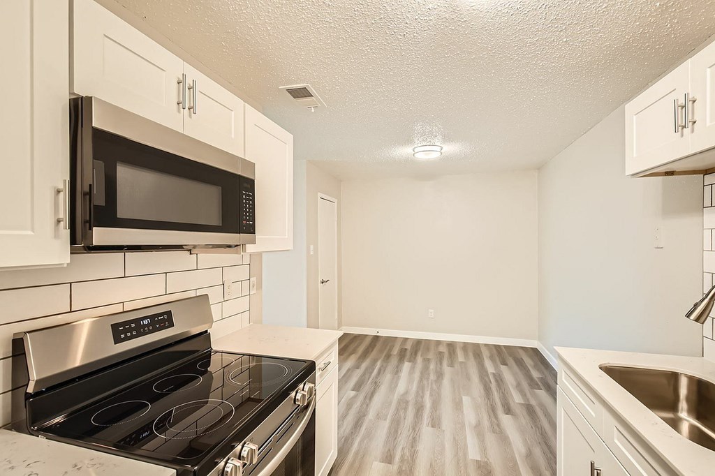 A kitchen with a black microwave above a stove and white cabinets.