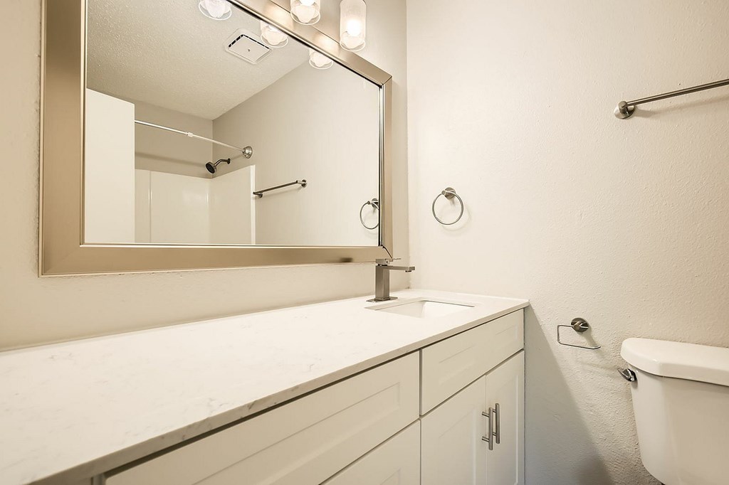 A white bathroom with a mirror, sink, and toilet.