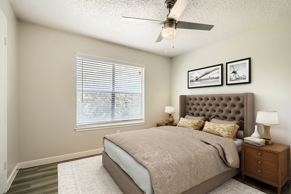 A bedroom with a large bed, a ceiling fan, and two framed pictures on the wall.