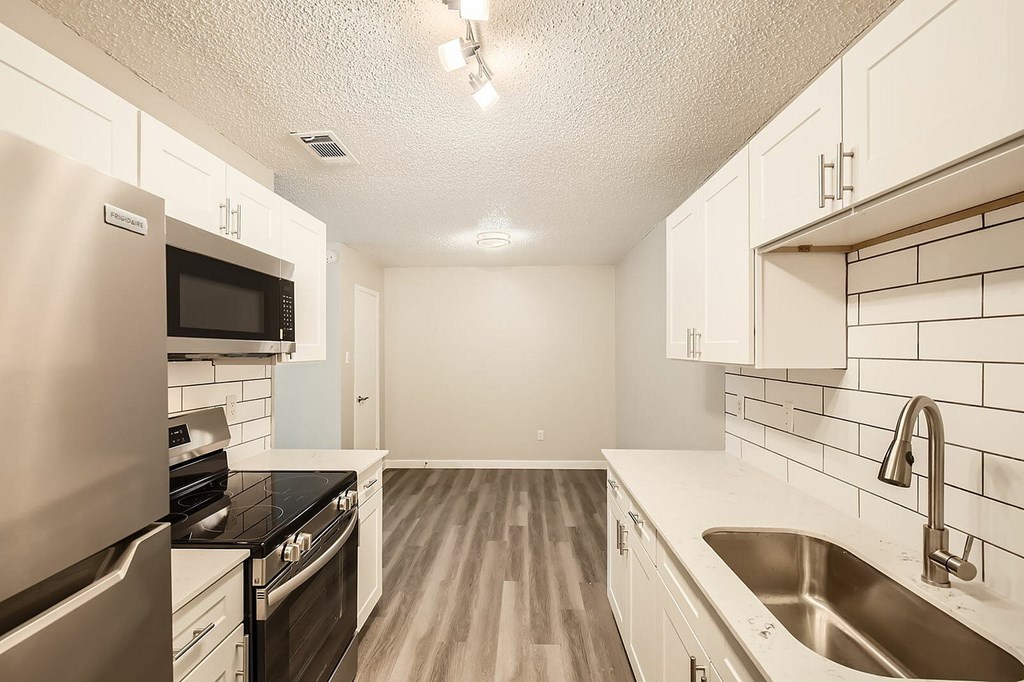 A kitchen with a stainless steel refrigerator, black countertops, and white cabinets.