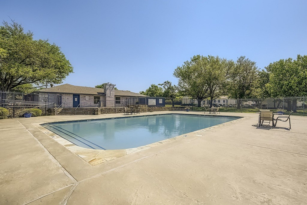 A large outdoor swimming pool surrounded by a concrete patio and a fence.