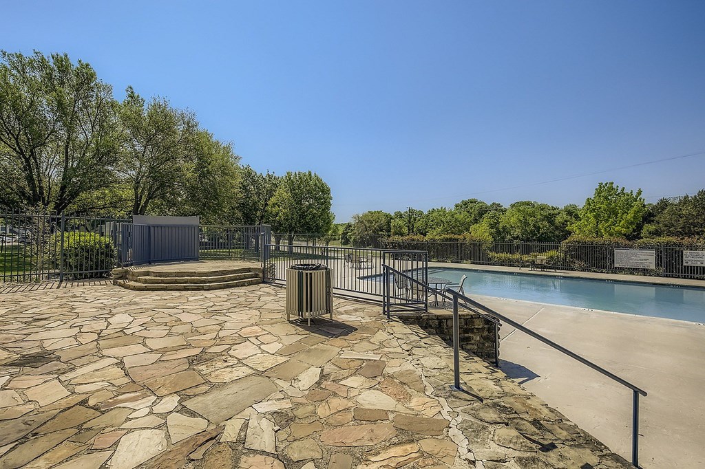 A pool area with a stone walkway and a metal fence.