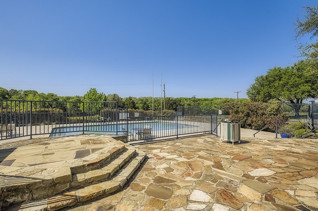 A pool surrounded by a stone patio and a metal fence.