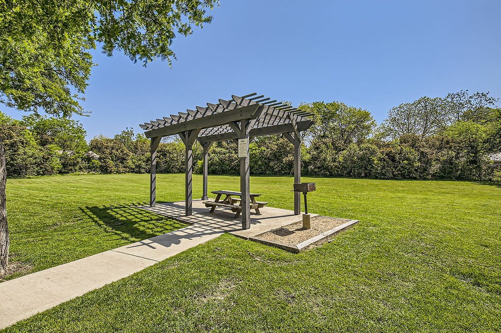 A picnic pavilion with a table and benches is situated in a grassy area.