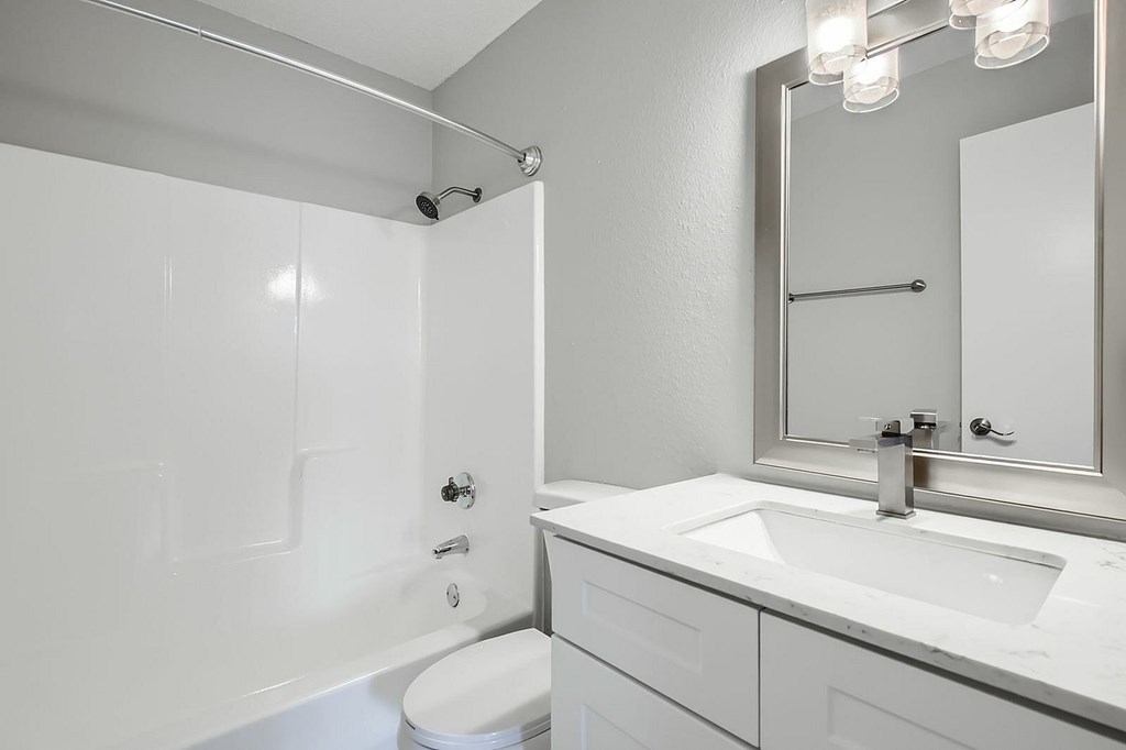 A white bathroom with a toilet, sink, and mirror.
