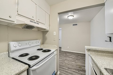 A kitchen with a white stove top oven and white cabinets.
