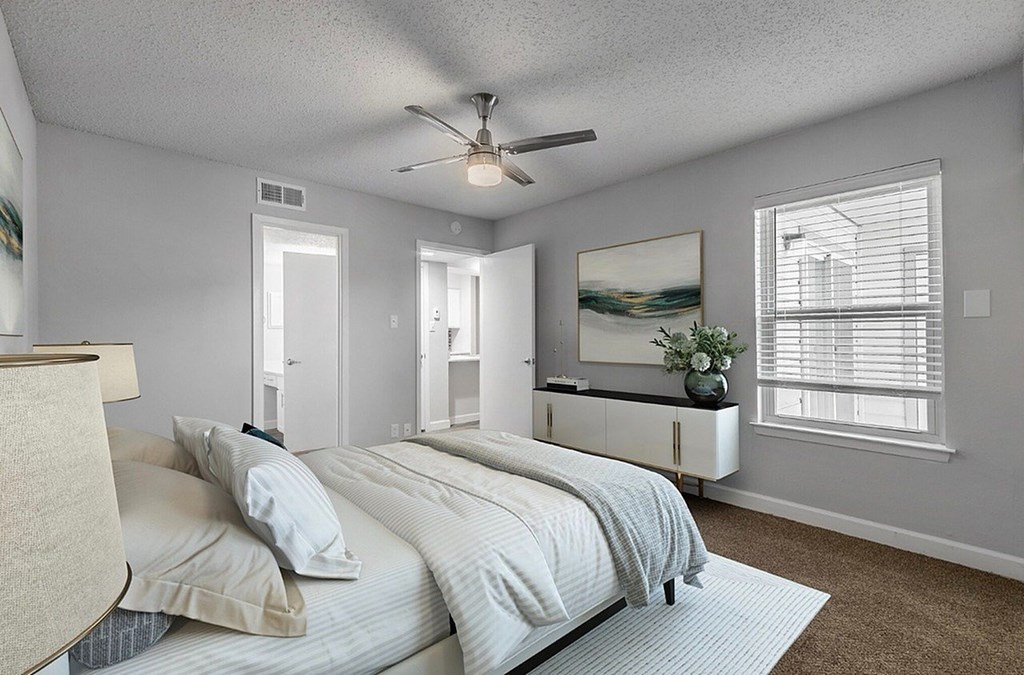 A bedroom with a bed, a ceiling fan, and a painting on the wall.