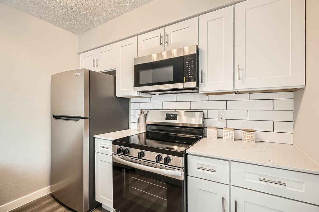 A kitchen with a stainless steel refrigerator, microwave, oven, and white cabinets.