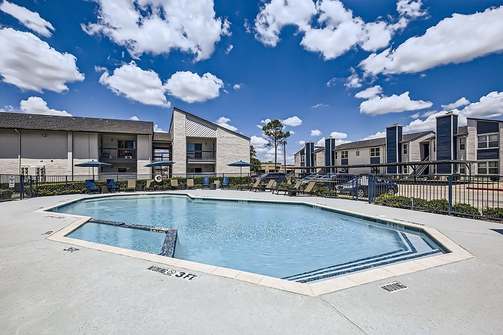 A swimming pool in front of a building with a blue sky and clouds in the background.