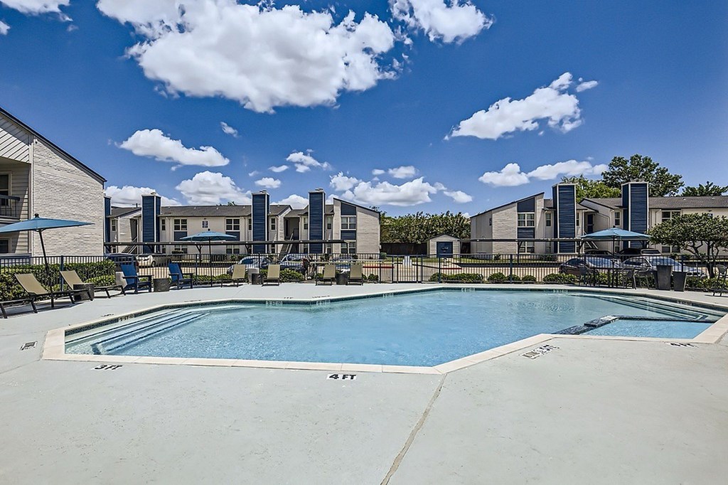 A swimming pool in front of a building with a blue sky and clouds in the background.