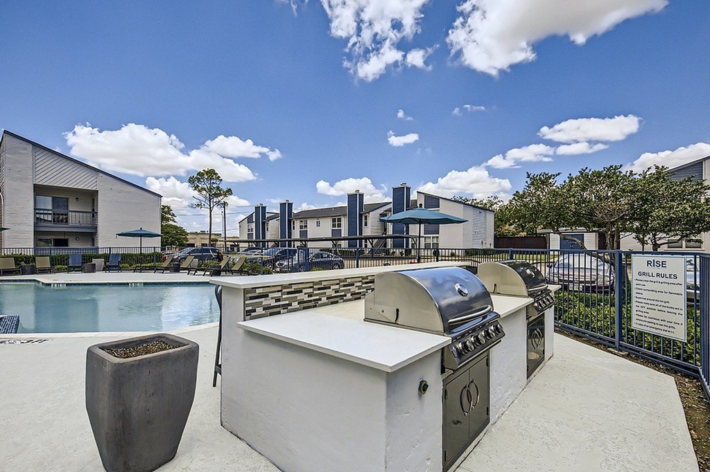 A sunny day at a poolside with a grill and a building in the background.