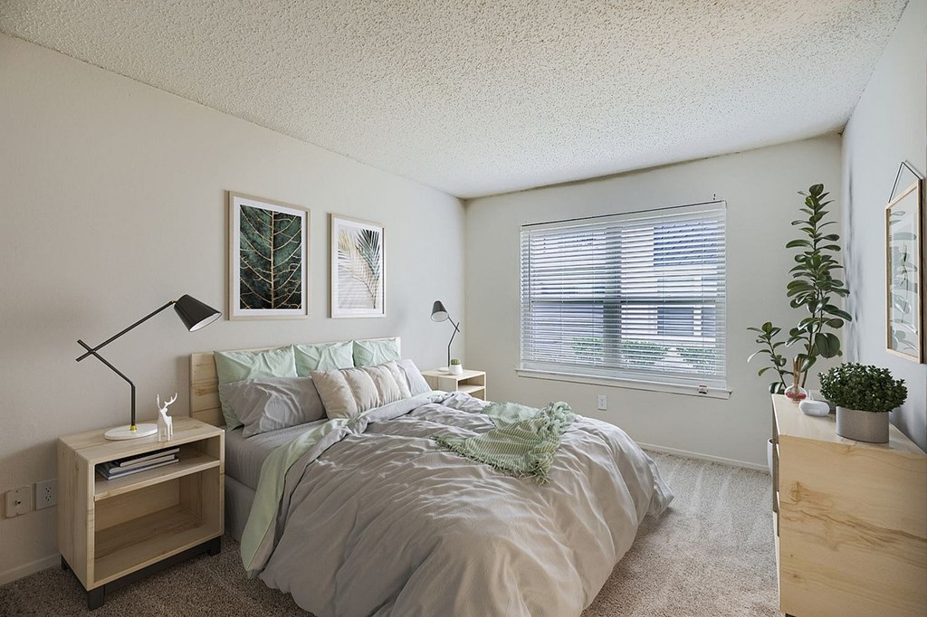 A bedroom with a bed, nightstand, and a plant.