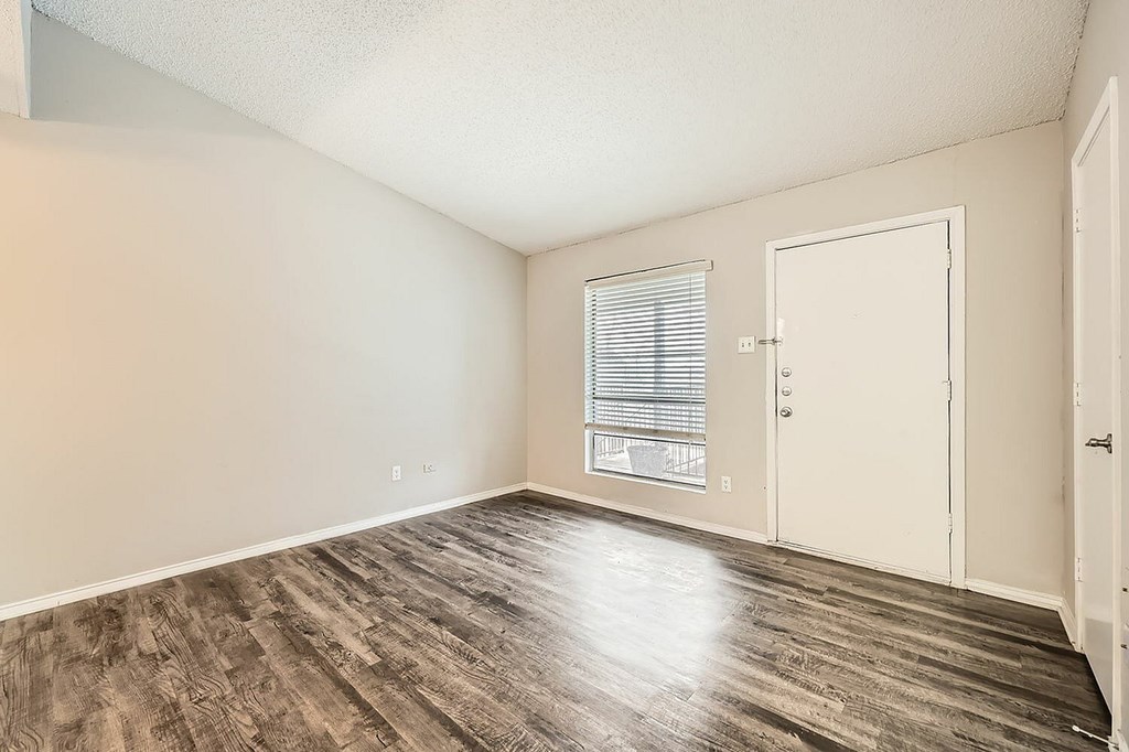 A room with a wooden floor and a window with blinds.