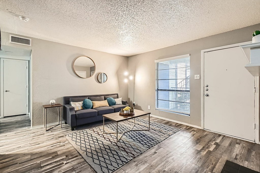 A living room with a grey couch and a round mirror on the wall.