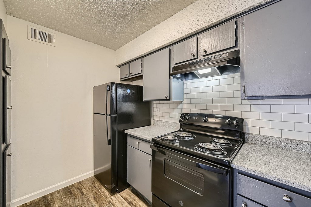 A black refrigerator and stove in a kitchen with white tiles.
