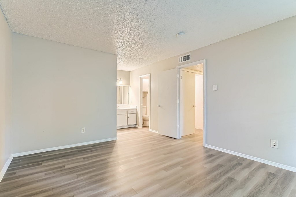 A room with a white ceiling and wooden flooring with a white door on the right.