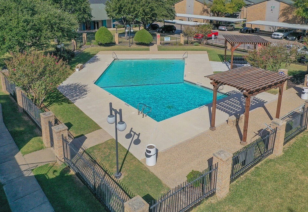 A pool with a wooden pergola and a fence surrounding it.