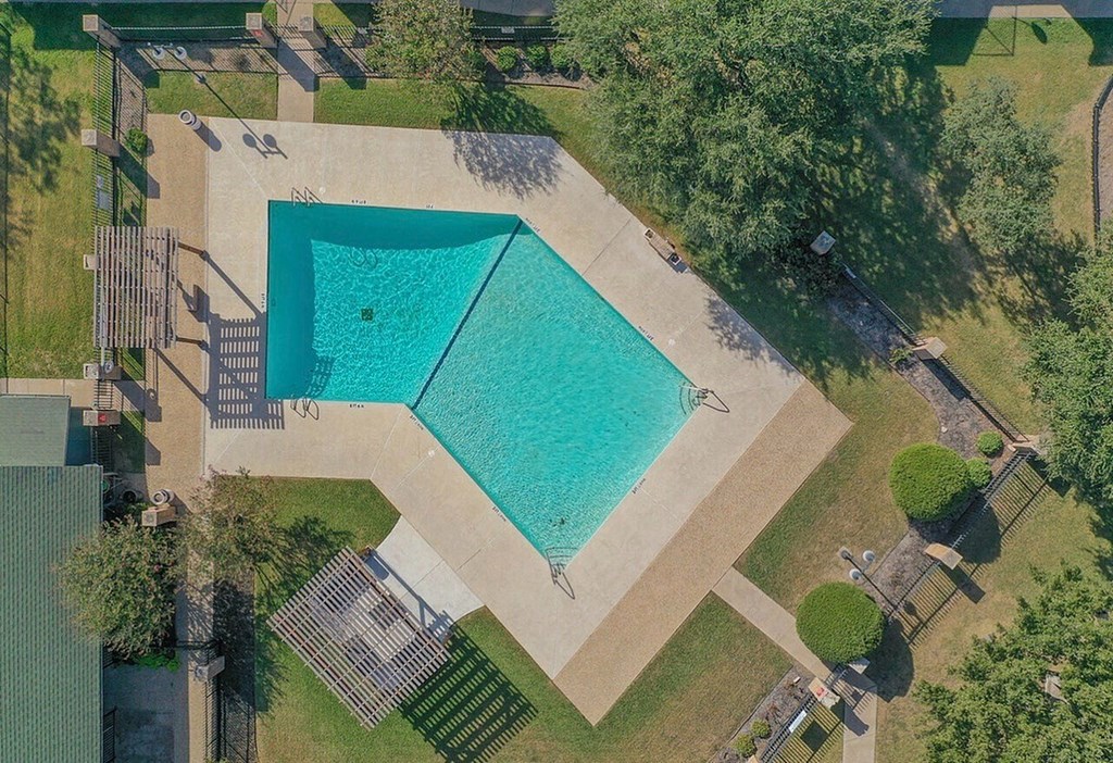 An aerial view of a swimming pool surrounded by a grassy area and trees.