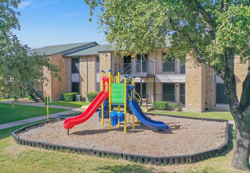 A playground with a red slide, a blue slide, and a yellow slide.