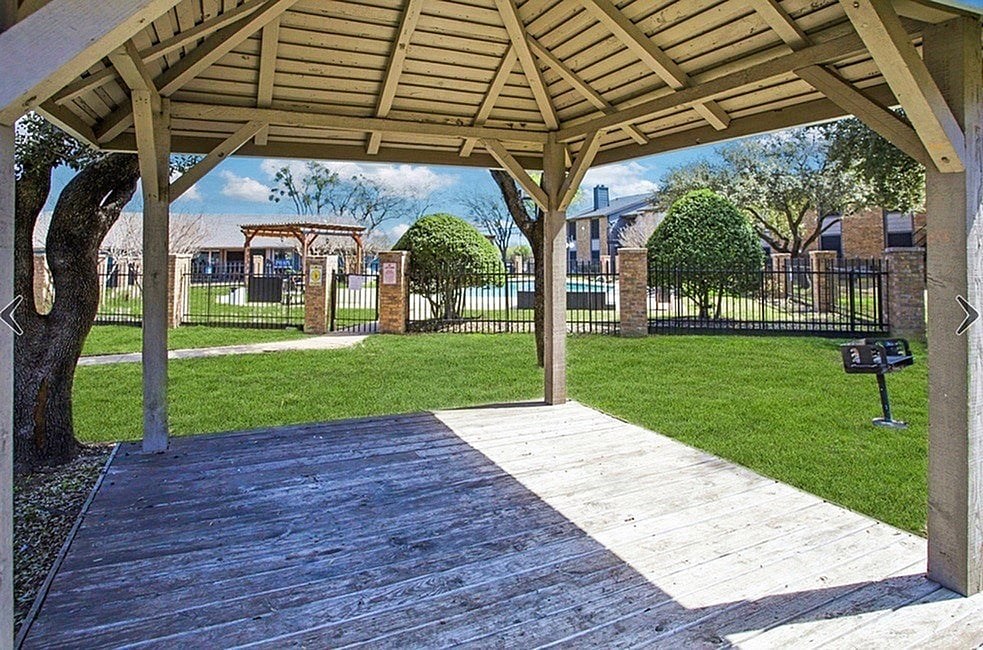 A wooden pavilion with a bench and a tree in the foreground.