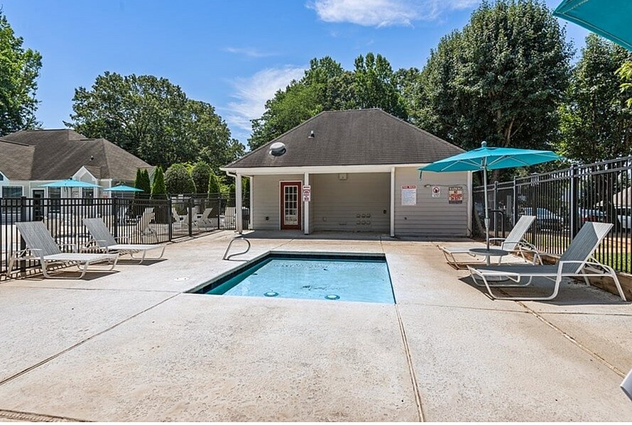 A pool area with a small building and lounge chairs.