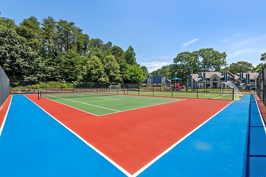 A tennis court with a red and blue surface surrounded by a fence.