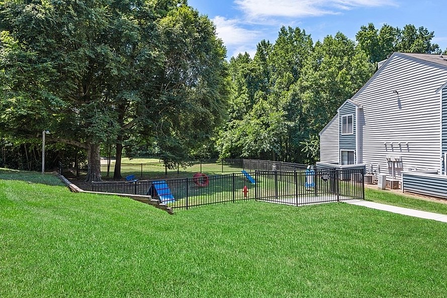 A backyard with a fence, a swing set, and a house.