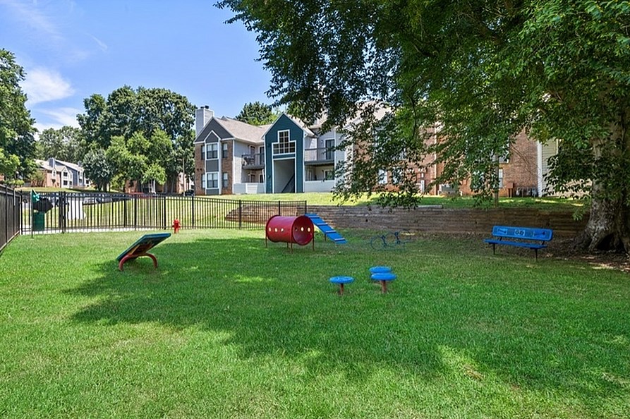A playground with a slide, swings, and a seesaw in a grassy area.