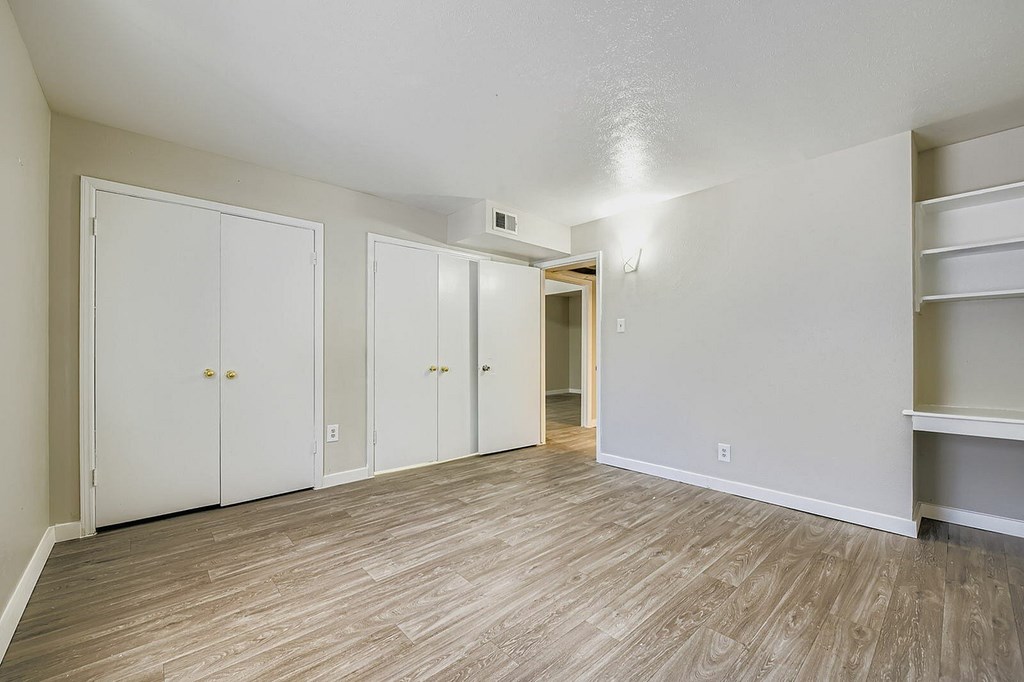 A room with white walls and wooden flooring with four doors.