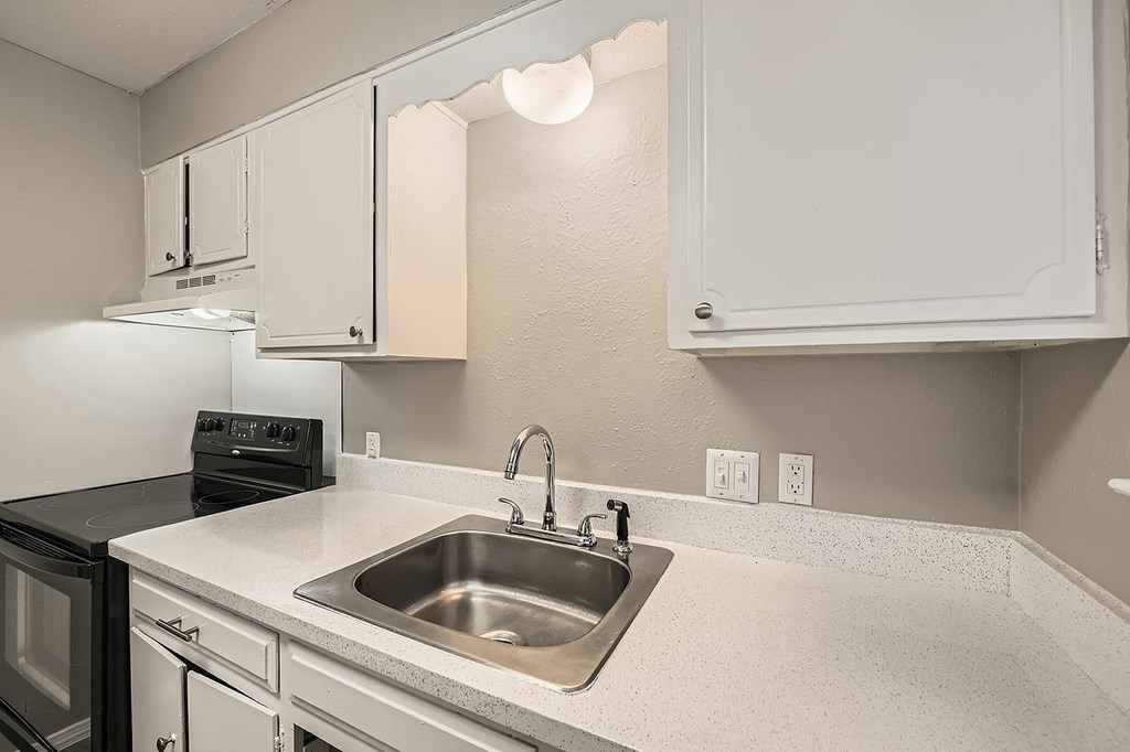 A kitchen with a sink, stove, and cabinets.