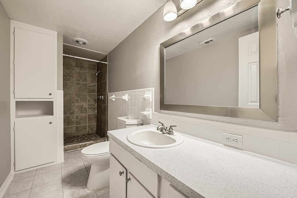 A bathroom with a toilet, sink, and mirror.