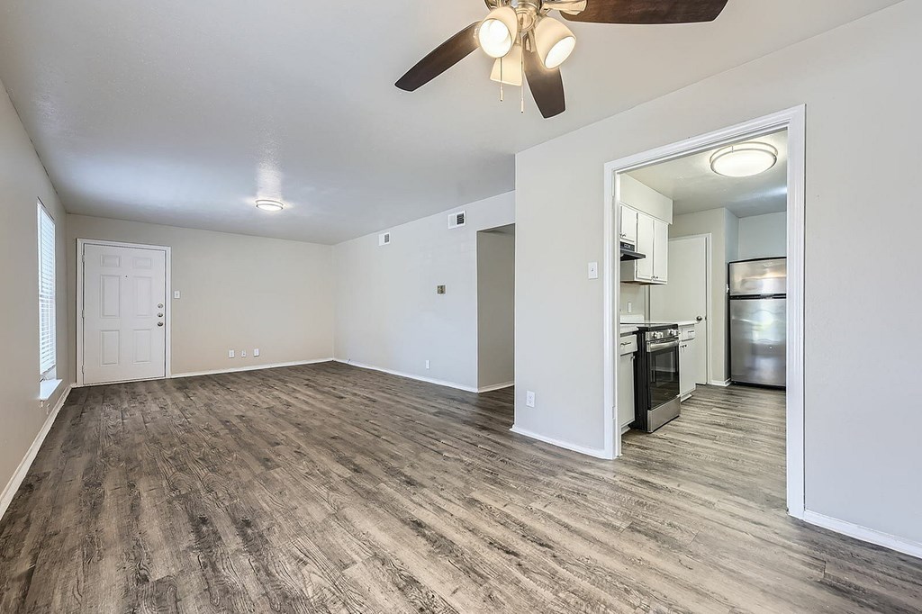 A room with a ceiling fan and a kitchen area in the background.
