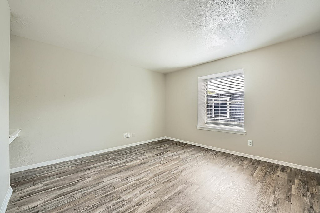 A room with wooden flooring and a window with blinds.