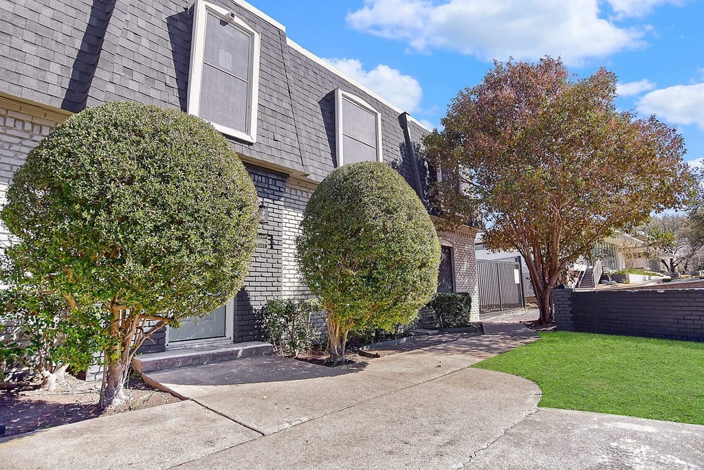 A house with a grey roof and a grey front yard with two bushes.