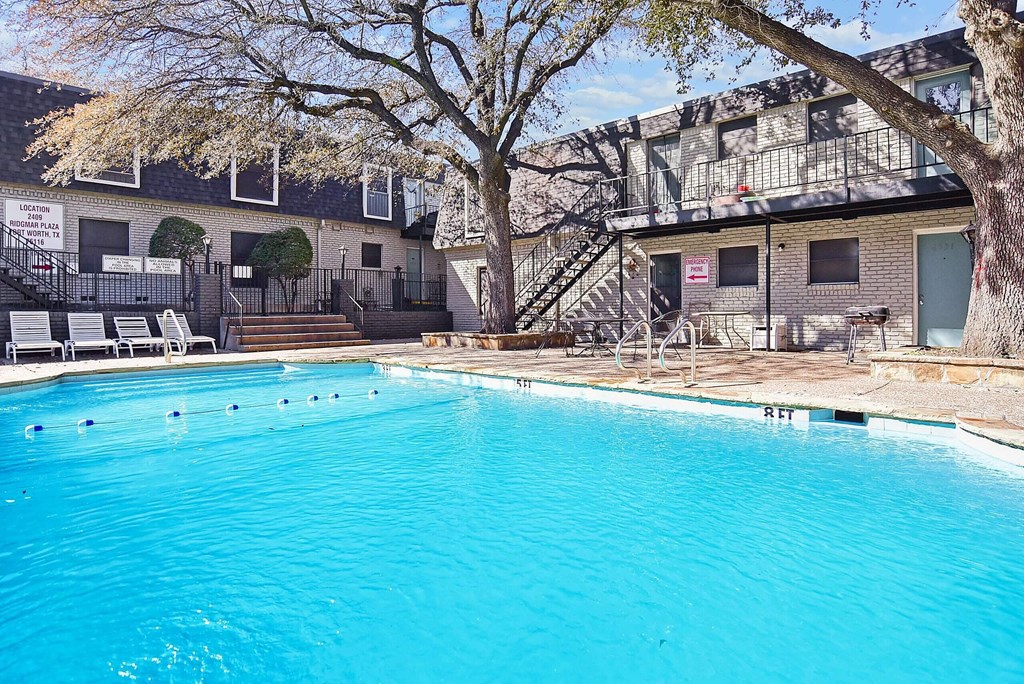 A swimming pool in front of a building with a tree on the left side.