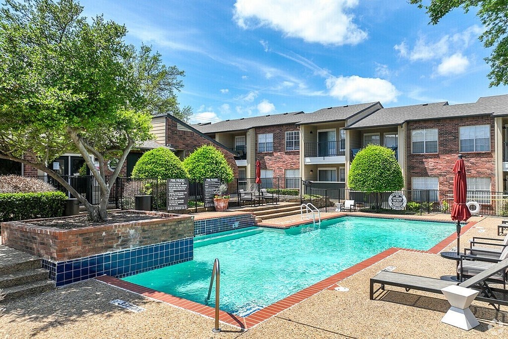 A swimming pool surrounded by a brick wall and lounge chairs.