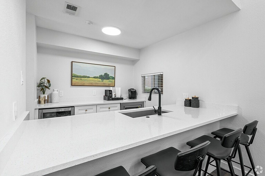 A kitchen with white countertops and black chairs.