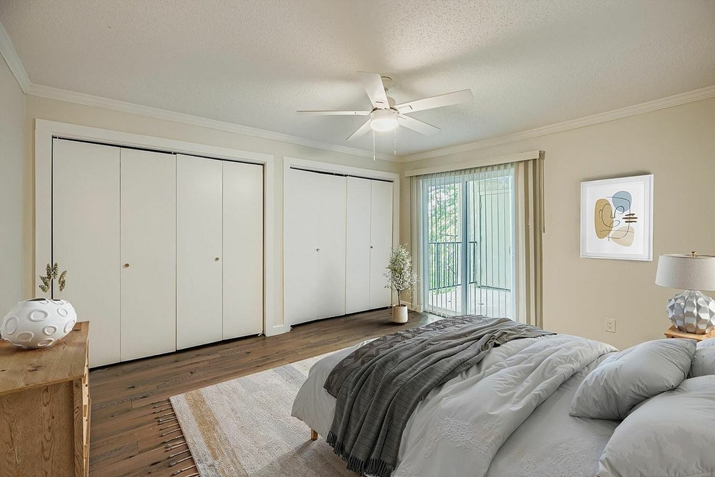 A bedroom with a bed, a ceiling fan, and a window with a view of a balcony.
