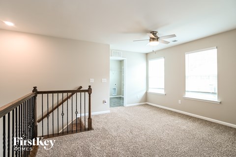 A spacious room with a carpeted floor, a ceiling fan, and a staircase with a railing.