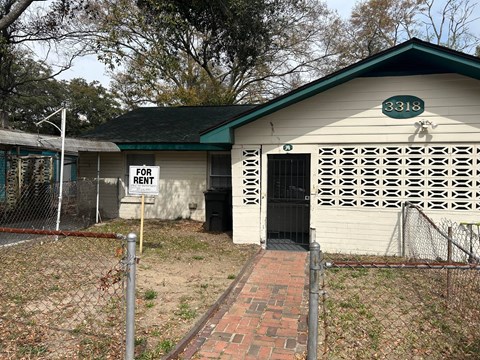 A white building with a green roof has a sign that says "FOR RENT" on it.