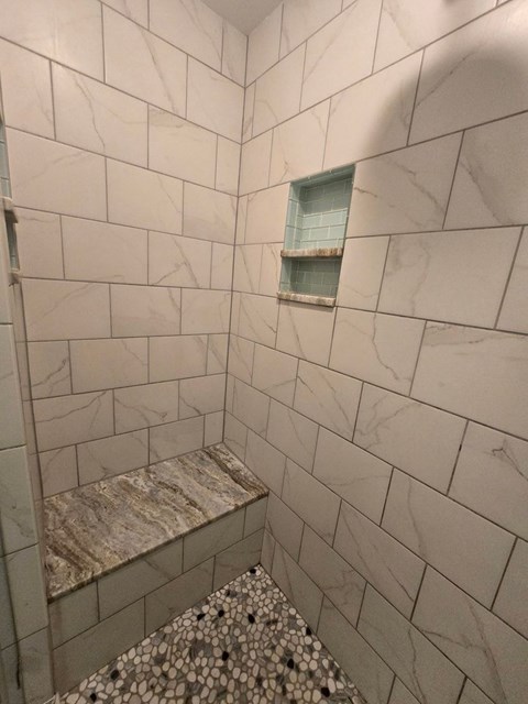 A bathroom with a marble tile shower and a window.