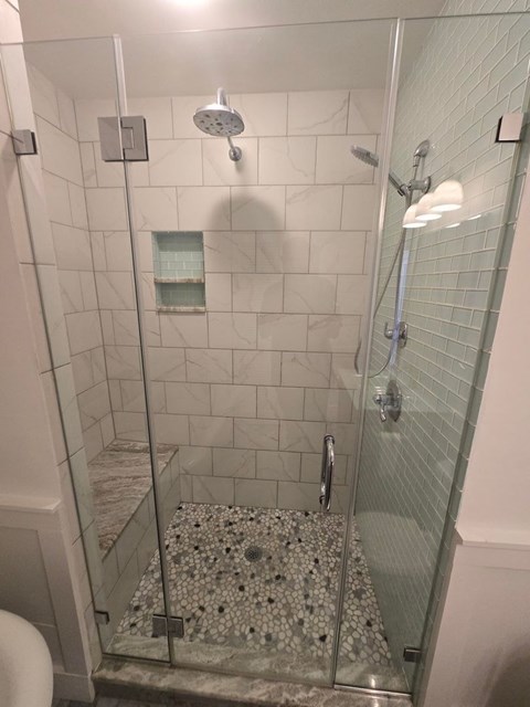 A shower with a glass door and a glass shelf.