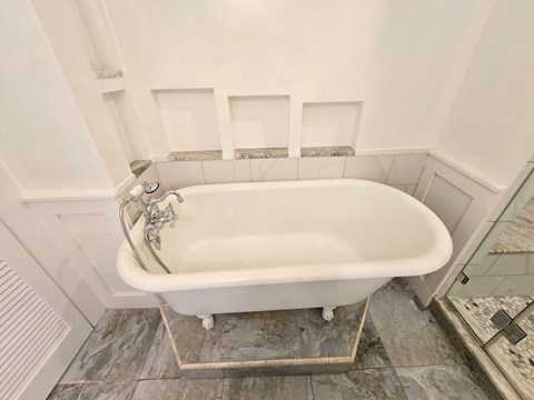 A white bathtub with a silver faucet is in a bathroom with a tiled floor.