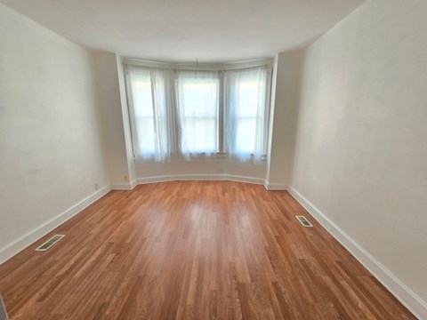 A room with wooden flooring and a window with white curtains.