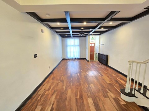 A room with wooden floors and a staircase on the right side.