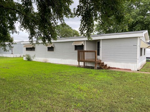 A mobile home with a porch and a tree in the foreground.